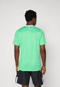 Zöld atlétikai rövid ujjú póló kerek nyakkal. Simább anyagból készült, fehér részlettel a gallérnál és logóval az ujjon.