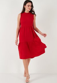Red, sleeveless dress with a fitted bodice and a tiered, flowing skirt. Soft texture, knee-length, featuring a round neckline and slight A-line shape.