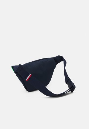 Borse a tracolla in tessuto blu navy con forma triangolare, caratterizzata da un accento verde, spallaccio regolabile e dettagli a strisce rosso, bianco e blu.