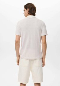 Lys beige polo skjorte med strikket tekstur og korte ærmer, parret med cremefarvede shorts. Enkel design, uden synlige mønstre eller accenter.