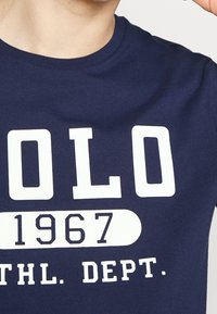 Navy blue cotton t-shirt featuring large white print: "POLO 1967" and "ATHL. DEPT." with a round neckline and short sleeves.
