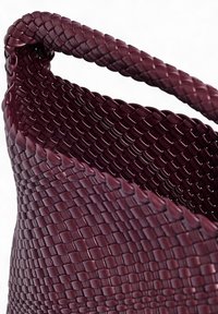 Vävd burgundyröd korg med en slät textur. Har ett robust handtag och en utvidgad öppning som visar upp tätt flätade detaljer genom hela korgen.