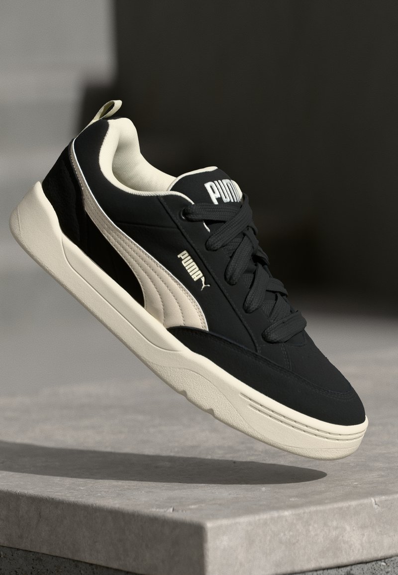 Mustvalge toss, millel on sile tekstuur, valge Puma logo ja sobivad paelad; omab pehmendatud krae ja kummist talla.