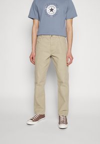 Khaki cotton trousers with straight legs and front pockets, paired with a blue graphic t-shirt featuring a circular white star logo.