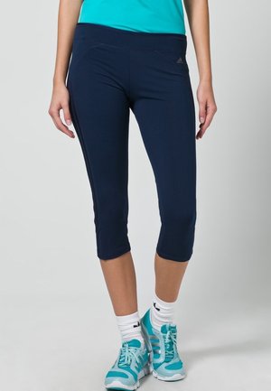Leggings capri atletici blu navy con una texture liscia, dotati di una cintura larga e dettagli di cucitura discreti. Abbinati a scarpe da ginnastica color teal.