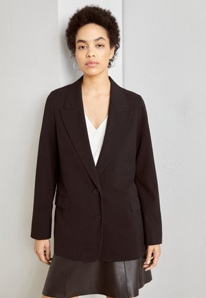 Blazer noir à la coupe ajustée, design à bouton unique, deux boutons et revers, assorti à un haut blanc et une jupe en cuir.