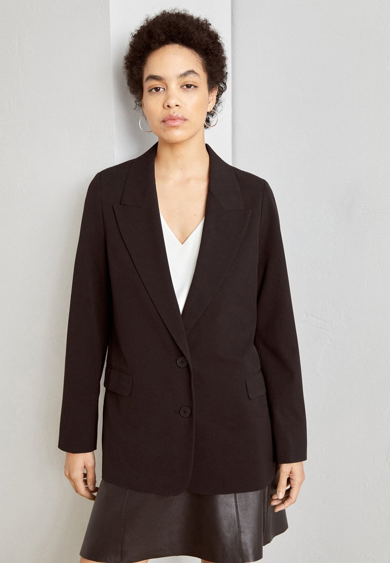 Blazer noir à la coupe ajustée, design à bouton unique, deux boutons et revers, assorti à un haut blanc et une jupe en cuir.