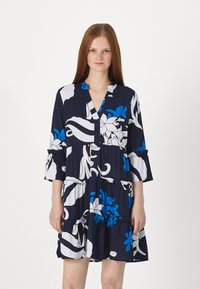 Vestido floral azul-marinho com padrões em branco e azul. Apresenta um decote em V, mangas três quartos e volantes em camadas na barra.