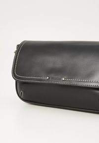 Borsa a pochette in pelle nera con chiusura a pattina, cuciture bianche a contrasto e piccoli dettagli metallici. Texture liscia con design minimalista.