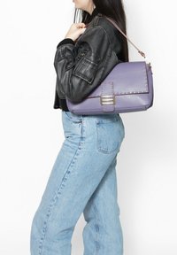 Borsa a tracolla in pelle viola con finitura testurizzata, dotata di patta pieghevole, accessori metallici e una tracolla marrone.