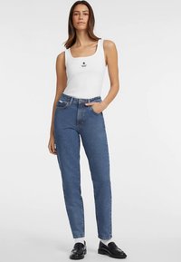 Valkoinen toppi, jossa musta tähtikuvio, yhdistetty korkeavyötäröisiin sinisiin farkkuihin, jotka ovat suorat lahkeet, ja tummat kengät.