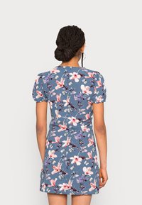 Vestido floral em tecido azul, com mangas curtas em puff, cintura ajustada, comprimento acima do joelho, com padrões de flores rosa e roxas.