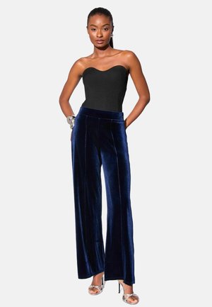 Black ribbed strapless top, blue velvet wide-leg pants with side seams, worn with silver high-heeled sandals.