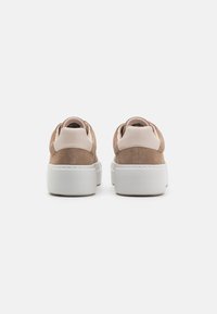 Beige Wildledersneaker mit einer weißen Plattformsohle, ausgestattet mit einer glatten pinken Ferse und einer gestickten Verzierung am Rand.