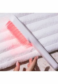 Dispositif de luminothérapie LED portatif blanc avec lumière rose sur une serviette blanche texturée, main avec des ongles manucurés à proximité.