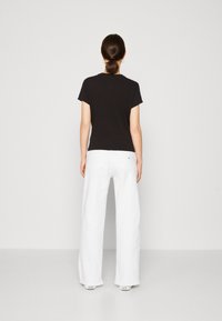 Černé tričko s krátkým rukávem v kombinaci s bílými širokými kalhotami. Oblečení má jednoduchý design a bavlněnou texturu. Na kalhotách je jemné logo.