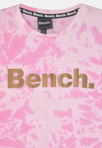 T-shirt em tie-dye rosa feito de algodão, com decote redondo e um grande logótipo dourado "Bench." ao centro, com uma textura suave.