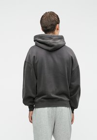 Sweatshirt oversized cinza escuro com capuz ajustável e punhos canelados, visto de trás. O material parece suave com uma textura lisa.