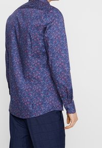 Koszula z długim rękawem wykonana z ciemnoniebieskiego materiału z kwiatowym wzorem w różowym i białym kolorze. Kołnierzyk zapięty na guziki oraz dopasowany krój z mankietami.
