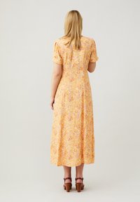 Vestido maxi amarillo con flores, manga corta con volantes, un cuerpo ajustado y una falda fluida. Presenta patrones florales en rosa y blanco.