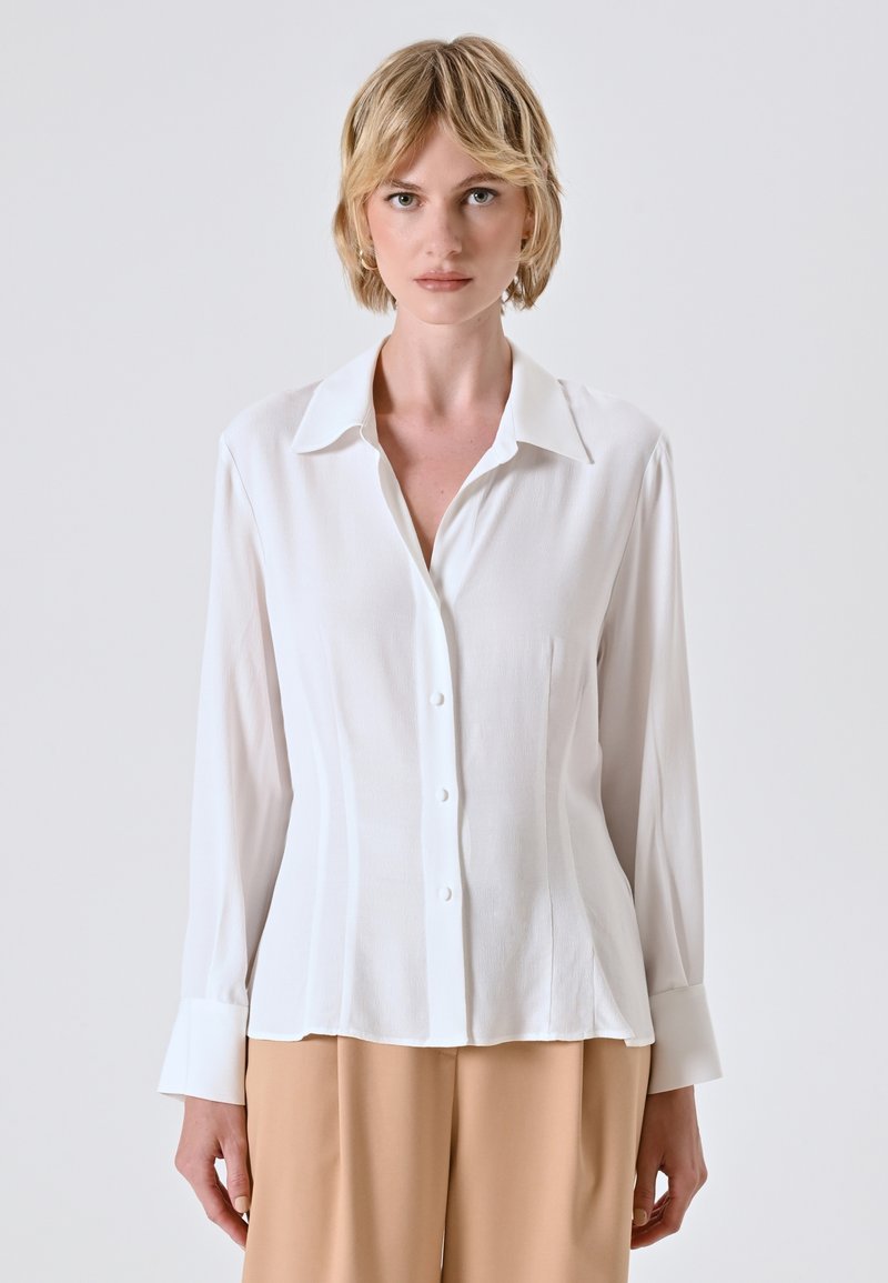 Witte overhemden met een klassieke kraag, lange mouwen en een getailleerde taille. Gladde textuur met subtiele verticale lijnen.