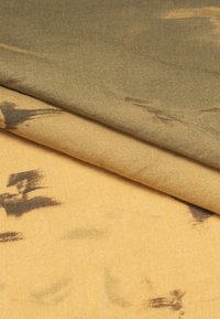 Due pezzi di tessuto sovrapposti: uno verde oliva con una texture morbida e liscia e uno giallo dorato con marcature scure astratte, entrambi leggeri.