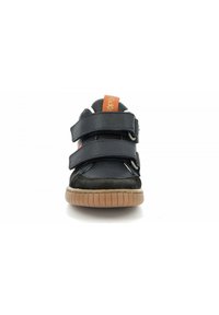 Scarpa sportiva nera con due cinturini in Velcro, suola in gomma, e un'etichetta arancione sulla parte superiore. Presenta una combinazione di materiali lisci e testurizzati.