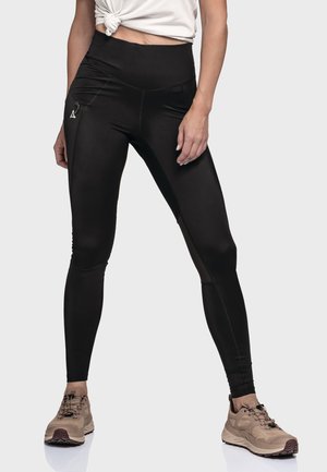 Black high-waisted leggings with a smooth texture, featuring a side zip pocket and flatlock seams, paired with tan athletic shoes.
