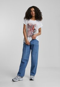 T-shirt graphique blanche avec un motif de bicyclette agrémenté d'éléments floraux, associé à un jean bleu ample et des baskets grises. Look décontracté et style.