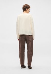 Ανοιχτό μπεζ πουλόβερ με χαμηλωμένους ώμους, συνδυασμένο με χαλαρά σκούρα καφέ παντελόνια. Η πίσω όψη αναδεικνύει την απαλή υφή και την απλότητα.