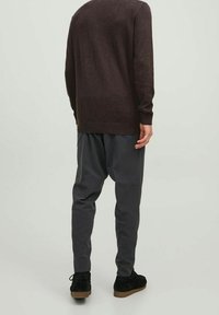Pull marron en tricot et pantalon gris fuselé, associés à des chaussures en daim noires. Texture douce, design décontracté, avec une coupe ample.