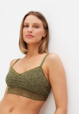 Bralette in pizzo verde oliva con spalline regolabili, bordo in pizzo a scallop e un piccolo fiocco al centro. Tessuto morbido e testurizzato.