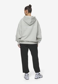 Light gray hoodie with a large back print "NO SPEED LMT" in white. Features a drawstring hood and oversized fit, paired with black trousers.