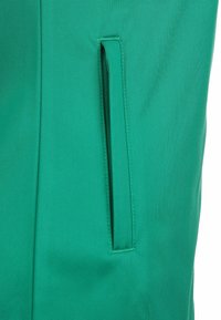 Groene stof met een gladde textuur heeft een zijzak met een verborgen rits, geïntegreerd in een gestroomlijnd ontwerp.