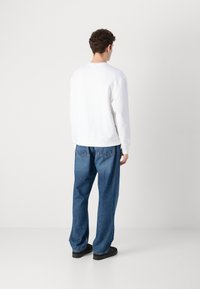 Sudadera blanca con cuello redondo, combinada con jeans de mezclilla azul sueltos. Los jeans tienen costuras visibles y un ajuste relajado. Unos zapatos negros completan el look.