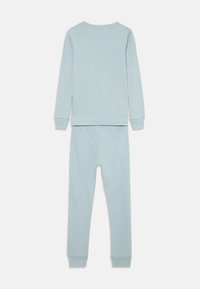 T-shirt bleu clair à manches longues et pantalon assorti avec des poignets élastiques, posés à plat sur un fond blanc, vue de dos.