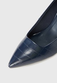 Décolleté punta rialzata di colore blu navy con motivo coccodrillo lucido, caratterizzata da un design elegante e una texture interna liscia.