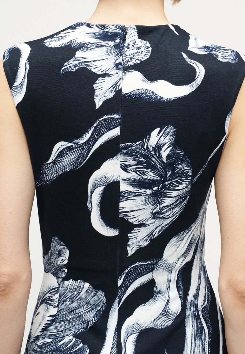 Back view of a sleeveless black dress with large white floral print and a visible central seam on the upper back.