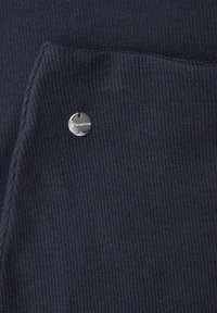 Donker marineblauw geribbeld stof met een omgevouwen hoek en een klein, rond zilveren label met de gravure "StreetOne".