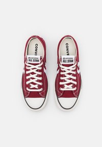 Rote Leinenschuhe mit weißen Schnürsenkeln, Gummizehenschutz und schwarzem Besatz. Verfügt über das "Converse All Star"-Logo auf der Zunge und den Seiten.