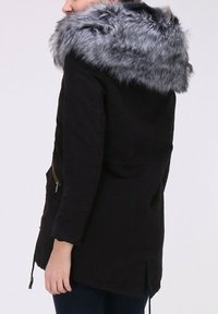 Veste noire avec une capuche doublée de fourrure grise, une poche zippée sur le côté et un dos plus long. Le tissu semble doux et texturé.