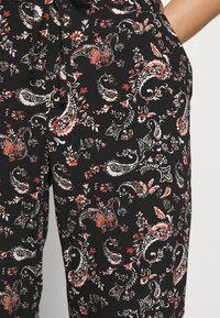 Black fabric pants with a colorful paisley pattern featuring red and white floral accents; includes a tied waistband detail.