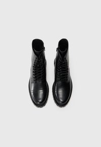 Botas de tobillo de cuero negro con punta redonda, cordones en la parte delantera y cremallera lateral. Textura suave con un detalle de costura mínimo.