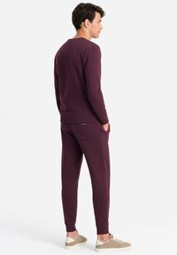 Bordeauxfarbener Baumwoll-Sweatshirt- und Jogginganzug mit gerippten Bündchen und Saum, seitlichen Taschen und einem kleinen Detail mit Rückentasche.
