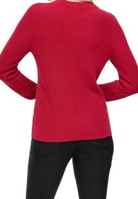 Pull rouge côtelé à manches longues et col rond, présentant une coupe ajustée. Porté avec un pantalon noir, vue de dos.