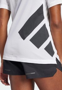 Camiseta atlética blanca de malla con patrones geométricos negros en la espalda, combinada con pantalones cortos negros que presentan acentos reflectantes en el dobladillo.