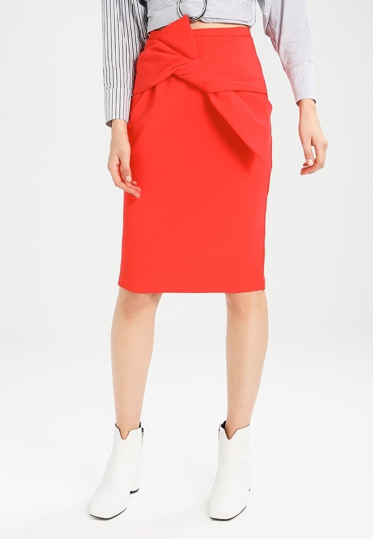 Femme portant une jupe rouge longueur genou avec un détail nœud à l'avant, un haut rayé à manches longues et des bottines blanches sur fond blanc.