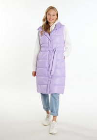 Vest padded de culoare violet deschis, cu o curea, cusături verticale și guler pliat, purtat peste un hanorac alb și asociat cu blugi denim cu manșete și adidași.