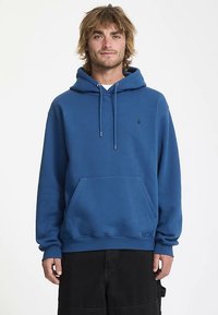 Blå hættetrøje lavet af bomuldsblanding, med en front kangurulomme, snore i hætten og et lille logo på brystet.