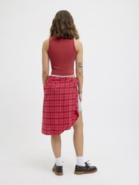 Piros bordázott crop top hosszú rózsaszín kockás szoknyával és farmernadrággal párosítva. Fekete cipők és fehér zoknik egészítik ki az öltözetet.
